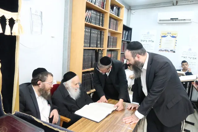 מרן נשיא המוסדות זצ״ל יושב על הספר בבית המדרש, בני הקהילה לומדים עמו